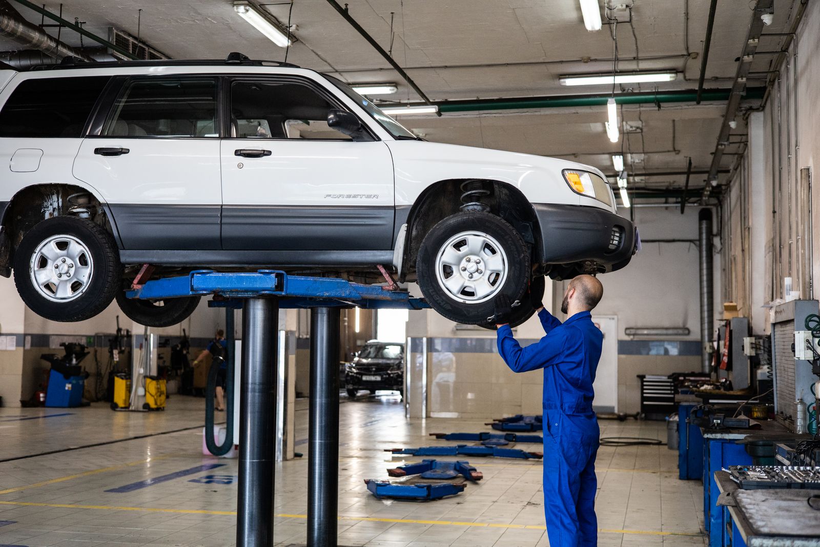 A technician working under a car raised on a lift in a service bay